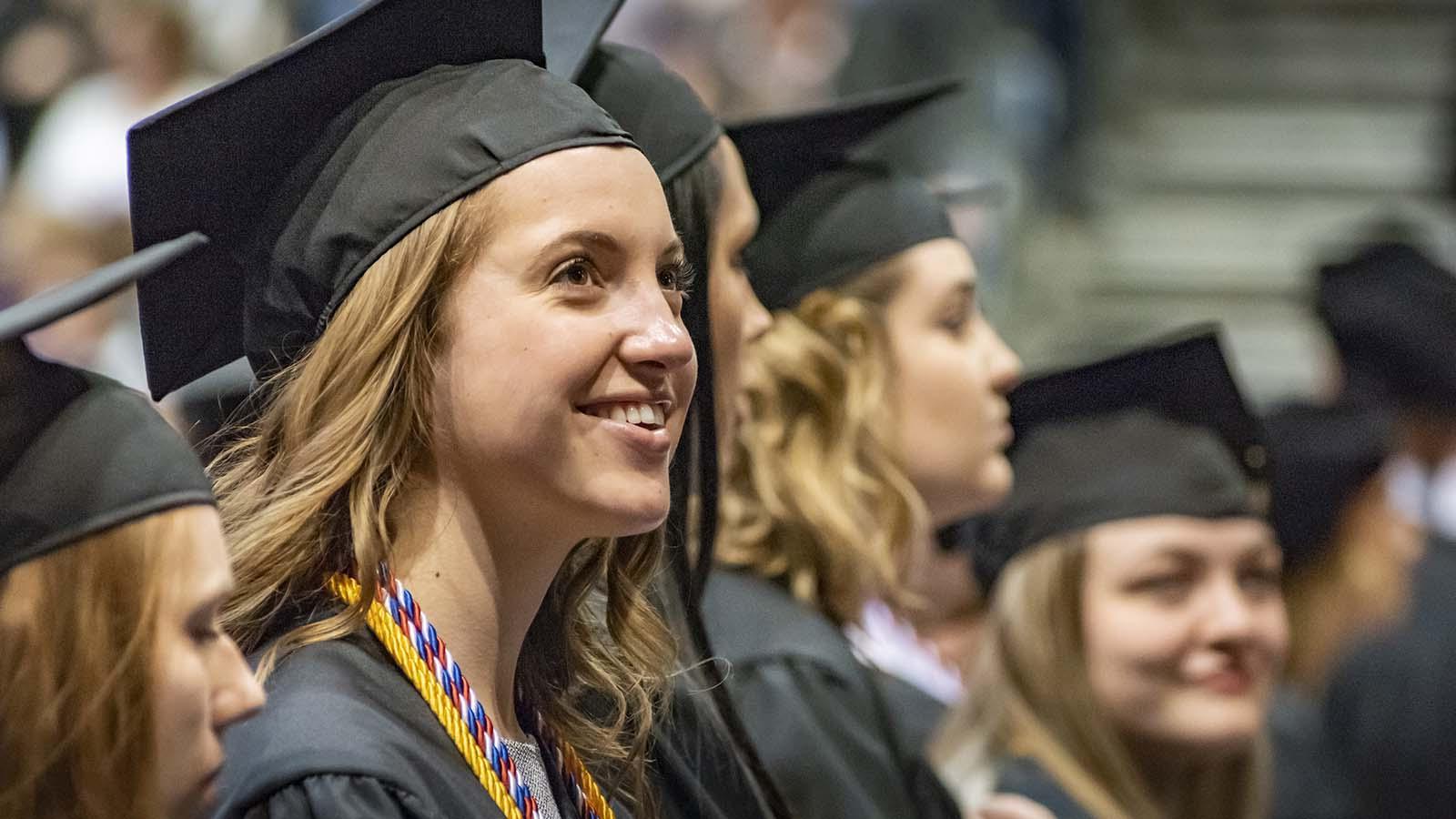 Happy female graduate at commencement with several students in the background.